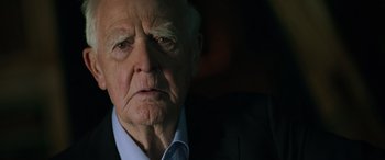Movie still from “The Pigeon Tunnel” (2023), directed by Errol Morris – An older man in a black suit and white shirt; Close Up shot, Over the shoulder angle