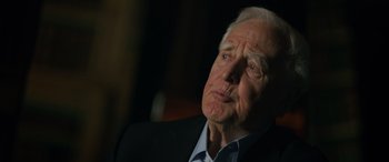 Movie still from “The Pigeon Tunnel” (2023), directed by Errol Morris – An older man wearing a suit and a white shirt; Close Up shot, Over the shoulder angle