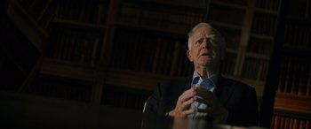 Movie still from “The Pigeon Tunnel” (2023), directed by Errol Morris – An older man sitting in front of a book shelf; Close Up shot, Low angle