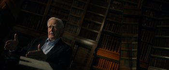 Movie still from “The Pigeon Tunnel” (2023), directed by Errol Morris – An older man in a suit in front of a book case; Medium shot, Low angle