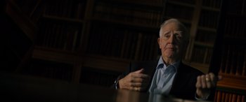 Movie still from “The Pigeon Tunnel” (2023), directed by Errol Morris – An older man sitting at a table in front of a book case; Close Up shot, Over the shoulder angle