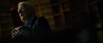 Movie still from “The Pigeon Tunnel” (2023), directed by Errol Morris – An older man sitting in front of a book shelf; Medium shot, Low angle