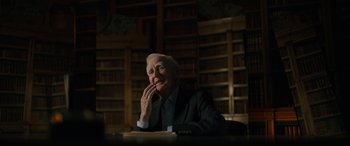 Movie still from “The Pigeon Tunnel” (2023), directed by Errol Morris – An older man sitting at a table in a library; Medium shot, Low angle