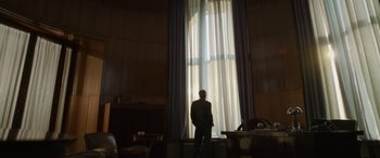 Movie still from “The Pigeon Tunnel” (2023), directed by Errol Morris – A man standing in front of a large window; Wide shot, Low angle