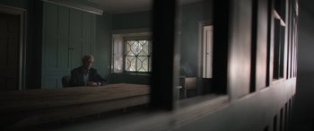 Movie still from “The Pigeon Tunnel” (2023), directed by Errol Morris – A man sitting on a bed in front of a window; Wide shot, Over the shoulder angle