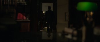 Movie still from “The Pigeon Tunnel” (2023), directed by Errol Morris – A man wearing a hat walking through a room; Wide shot, Over the shoulder angle