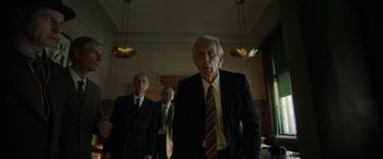 Movie still from “The Pigeon Tunnel” (2023), directed by Errol Morris – A group of men standing next to each other in a room; Medium shot, Low angle