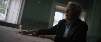 Movie still from “The Pigeon Tunnel” (2023), directed by Errol Morris – An older man sitting at a wooden table in front of a window; Close Up shot, Low angle