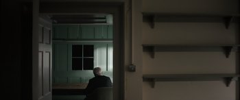 Movie still from “The Pigeon Tunnel” (2023), directed by Errol Morris – An older man sitting in a chair looking out a window; Wide shot, Low angle