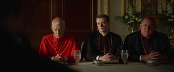 Movie still from “The Pope's Exorcist” (2023), directed by Julius Avery – A priest and a priest sitting at a table; Medium shot, Over the shoulder angle