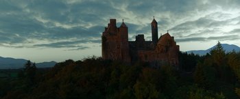 Movie still from “The Pope's Exorcist” (2023), directed by Julius Avery – A castle with a clock tower on top of a hill; Extreme Wide shot, Low angle
