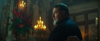 Movie still from “The Pope's Exorcist” (2023), directed by Julius Avery – A man sitting in front of candles in a room; Close Up shot, Low angle
