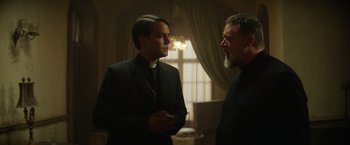 Movie still from “The Pope's Exorcist” (2023), directed by Julius Avery – A priest and a man talking in front of a window; Medium shot, Low angle