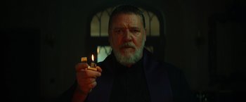 Movie still from “The Pope's Exorcist” (2023), directed by Julius Avery – An older man holding a lit candle in a dark room; Close Up shot, Low angle