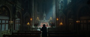 Movie still from “The Pope's Exorcist” (2023), directed by Julius Avery – Two people sitting in front of a church alter; Extreme Wide shot, Low angle