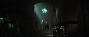 Movie still from “The Pope's Exorcist” (2023), directed by Julius Avery – Two people are sitting on some steps in a dark room; Extreme Wide shot, Low angle