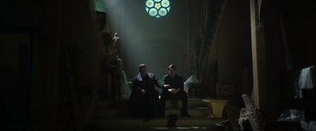 Movie still from “The Pope's Exorcist” (2023), directed by Julius Avery – A couple of men sitting next to each other on some steps; Wide shot, Low angle