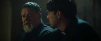 Movie still from “The Pope's Exorcist” (2023), directed by Julius Avery – Two men sitting next to each other in a dark room; Close Up shot, Over the shoulder angle