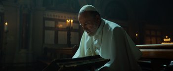 Movie still from “The Pope's Exorcist” (2023), directed by Julius Avery – A man in a priest's outfit looking down at a book; Close Up shot, Low angle