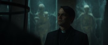 Movie still from “The Pope's Exorcist” (2023), directed by Julius Avery – A man wearing a priest's outfit looking up at a statue; Medium shot, Low angle