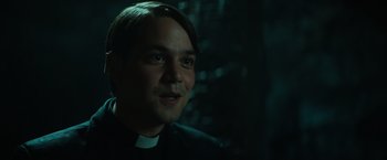 Movie still from “The Pope's Exorcist” (2023), directed by Julius Avery – A man in a priest's outfit is smiling for the camera; Close Up shot, Low angle