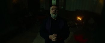 Movie still from “The Pope's Exorcist” (2023), directed by Julius Avery – An old man with a beard and a beard is standing in a dark room; Medium shot, Low angle