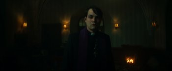 Movie still from “The Pope's Exorcist” (2023), directed by Julius Avery – A man wearing a priest's outfit with a cross on his neck; Medium shot, Low angle