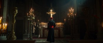 Movie still from “The Pope's Exorcist” (2023), directed by Julius Avery – A priest standing in front of a crucifixion; Extreme Wide shot, Low angle