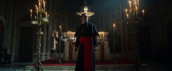 Movie still from “The Pope's Exorcist” (2023), directed by Julius Avery – A man in a priest's outfit stands in front of the alter; Medium shot, Low angle