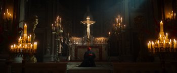 Movie still from “The Pope's Exorcist” (2023), directed by Julius Avery – A man sitting in front of a crucifixion in a church; Extreme Wide shot, Low angle