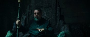 Movie still from “The Pope's Exorcist” (2023), directed by Julius Avery – An older man in a green suit is sitting in front of a stone wall; Medium shot, High angle