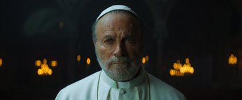 Movie still from “The Pope's Exorcist” (2023), directed by Julius Avery – An older man with a beard wearing a white hat; Close Up shot, Low angle