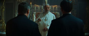 Movie still from “The Pope's Exorcist” (2023), directed by Julius Avery – An old man wearing a white robe and a cross in his hand; Medium shot, Over the shoulder angle