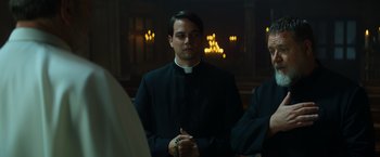 Movie still from “The Pope's Exorcist” (2023), directed by Julius Avery – A man wearing a priest's outfit standing in a church; Medium shot, Over the shoulder angle