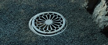 Movie still from “The Portable Door” (2023), directed by Jeffrey Walker – A metal vent on the ground; Extreme Close Up shot, Overhead angle