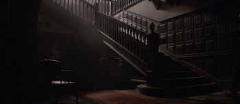 Movie still from “The Power of the Dog” (2021), directed by Jane Campion – A dark staircase with a person sitting on the bottom of it; Wide shot, Low angle