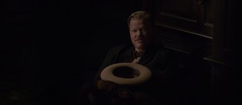 Movie still from “The Power of the Dog” (2021), directed by Jane Campion – A man in a suit and tie holding an object in his hand; Medium shot, High angle