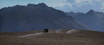 Movie still from “The Power of the Dog” (2021), directed by Jane Campion – An old car driving down a dirt road in the middle of the desert; Extreme Wide shot, High angle