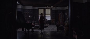 Movie still from “The Power of the Dog” (2021), directed by Jane Campion – A woman standing in a dark room in front of a window; Extreme Wide shot, High angle