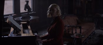 Movie still from “The Power of the Dog” (2021), directed by Jane Campion – A woman in a red jacket is playing the piano; Medium shot, Over the shoulder angle