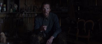 Movie still from “The Power of the Dog” (2021), directed by Jane Campion – A man sitting in a dark room holding a cigarette; Medium shot, Low angle