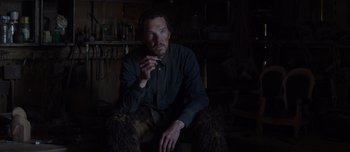 Movie still from “The Power of the Dog” (2021), directed by Jane Campion – A man sitting in a dark room holding a cigarette; Medium shot, High angle