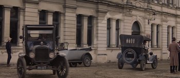 Movie still from “The Power of the Dog” (2021), directed by Jane Campion – Two antique cars parked in front of a building; Extreme Wide shot, High angle