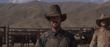 Movie still from “The Power of the Dog” (2021), directed by Jane Campion – A man wearing a hat standing in front of cows; Medium shot, Low angle