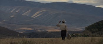 Movie still from “The Power of the Dog” (2021), directed by Jane Campion – A man in a cowboy hat is walking through a field; Extreme Wide shot, Low angle