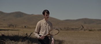 Movie still from “The Power of the Dog” (2021), directed by Jane Campion – A man holding a tennis racquet in a field; Medium shot, Low angle