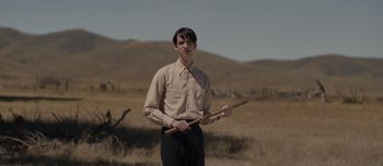 Movie still from “The Power of the Dog” (2021), directed by Jane Campion – A man holding a wooden stick in the middle of a field; Medium shot, Low angle