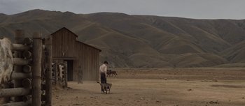 Movie still from “The Power of the Dog” (2021), directed by Jane Campion – A man standing in a dirt field next to a horse; Extreme Wide shot, Low angle