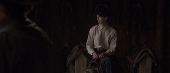 Movie still from “The Power of the Dog” (2021), directed by Jane Campion – A man sitting on a chair in front of a wall; Medium shot, Over the shoulder angle