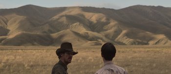 Movie still from “The Power of the Dog” (2021), directed by Jane Campion – Two men standing in front of a field with mountains in the background; Medium shot, Over the shoulder angle